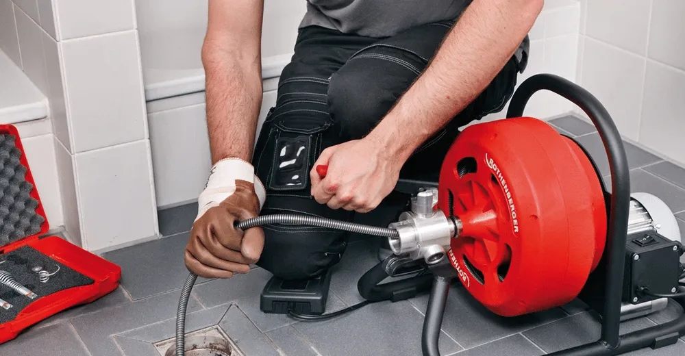 Main fermant une vanne d'équerre sous un lavabo, seau posé dessous